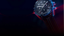 Luxury men's chronograph watch with black dial and brown leather strap, illuminated side view
